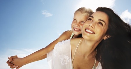 Little daughter enjoying a piggy back ride on mother on a sunny day